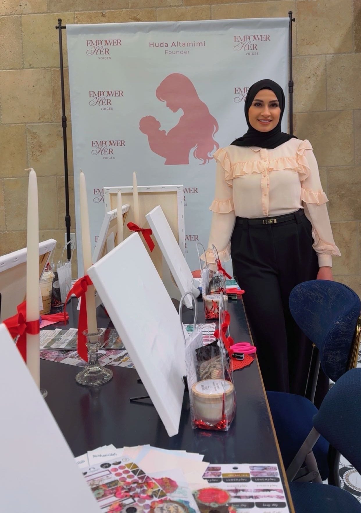 Huda Altamimi at an EmpowerHer Voices event, beside her branded banner and a vision-board table